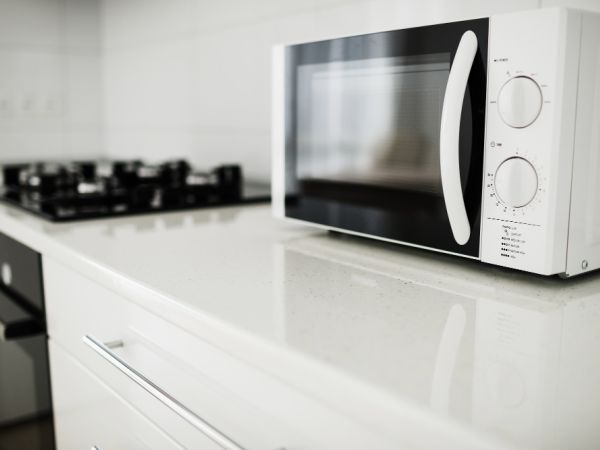 white microwave on a light coloure counter , it is sitting next to a hob