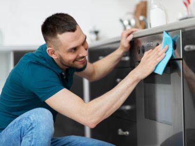 Man with rag cleaning oven door at home kitchen