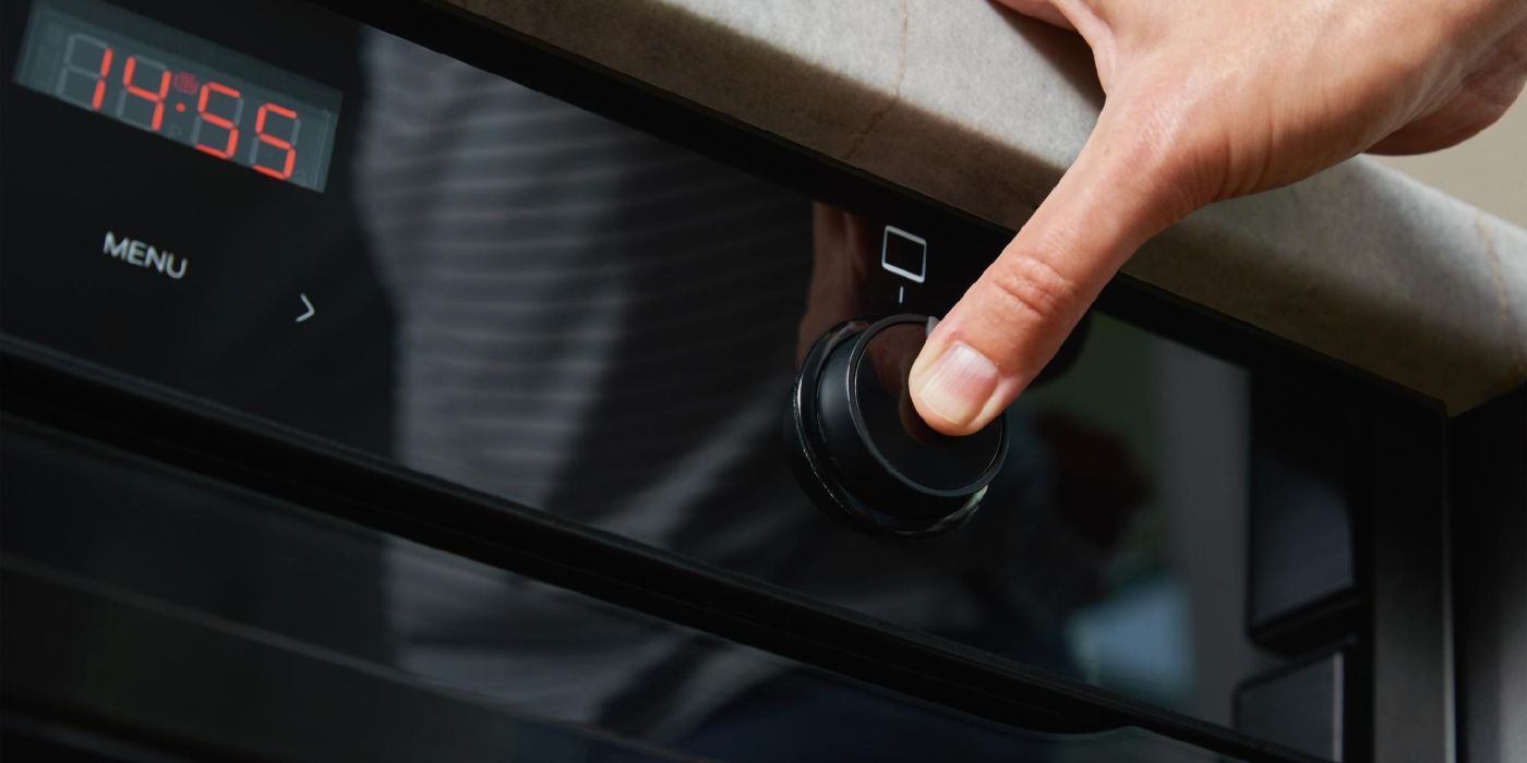 A person's hand pressing a button on an oven, there is a clock shown, the oven is black