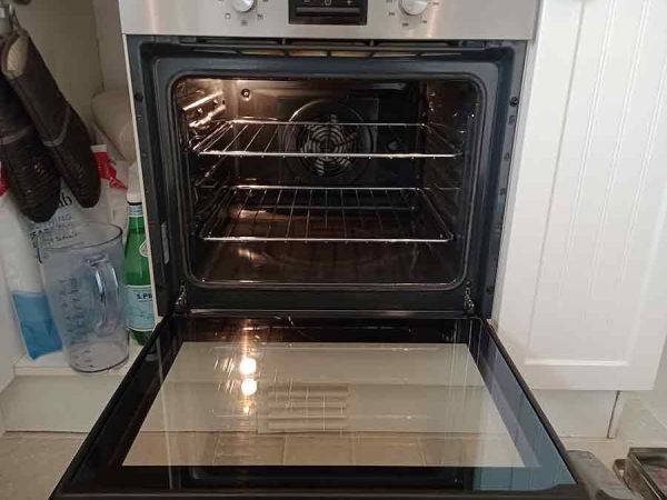 an oven with its door open, it is clean and there are some cleaning materials on the left